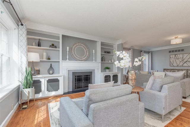 living room featuring visible vents, a textured ceiling, a glass covered fireplace, wood finished floors, and crown molding