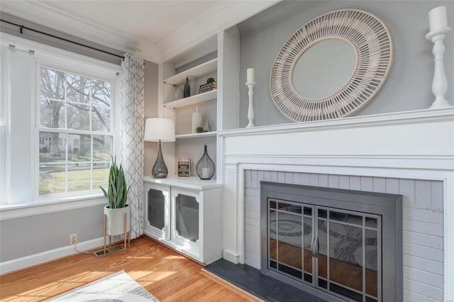 interior space featuring visible vents, a brick fireplace, baseboards, ornamental molding, and wood finished floors