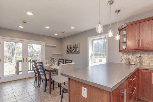 kitchen featuring tasteful backsplash, french doors, a peninsula, brown cabinetry, and hanging light fixtures