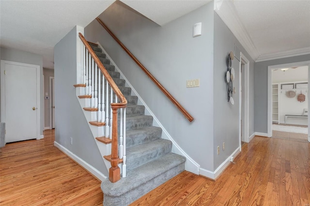 staircase featuring baseboards, a textured ceiling, wood finished floors, and crown molding