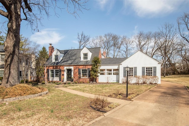 cape cod house with driveway, a chimney, and a front yard