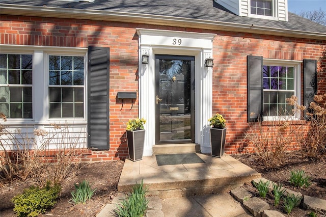 doorway to property with brick siding and roof with shingles