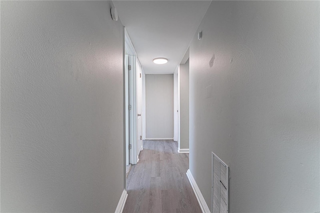 hallway with a textured wall, baseboards, visible vents, and light wood finished floors