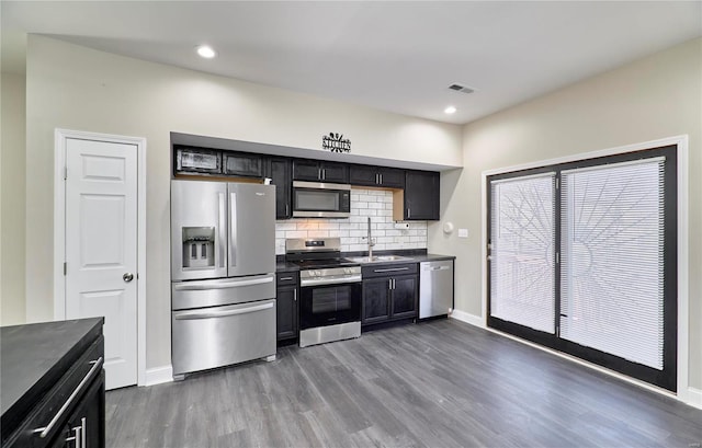 kitchen featuring dark wood-style flooring, a sink, stainless steel appliances, dark countertops, and tasteful backsplash