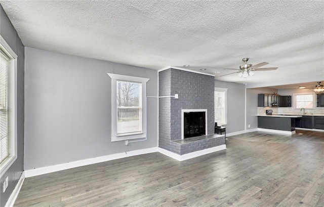 unfurnished living room with a brick fireplace, baseboards, ceiling fan, wood finished floors, and a sink