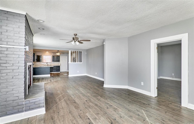 unfurnished living room featuring a brick fireplace, baseboards, and dark wood-style flooring