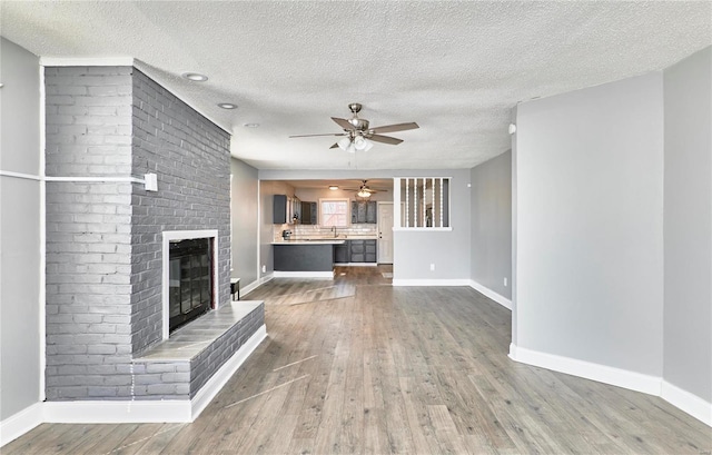 unfurnished living room featuring ceiling fan, baseboards, wood finished floors, and a fireplace