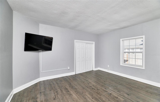 unfurnished bedroom featuring dark wood-type flooring, baseboards, a closet, and a textured ceiling