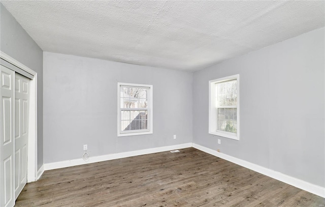 unfurnished bedroom with a closet, multiple windows, baseboards, and wood finished floors