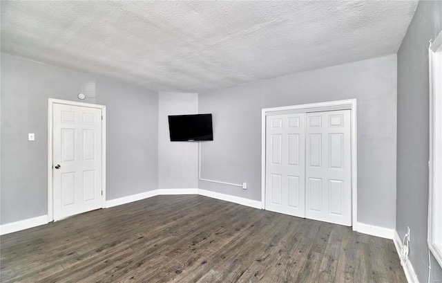 unfurnished bedroom featuring a closet, a textured ceiling, dark wood-type flooring, and baseboards