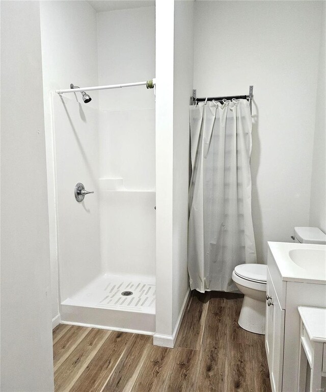 bathroom with a shower with shower curtain, wood finished floors, toilet, and vanity