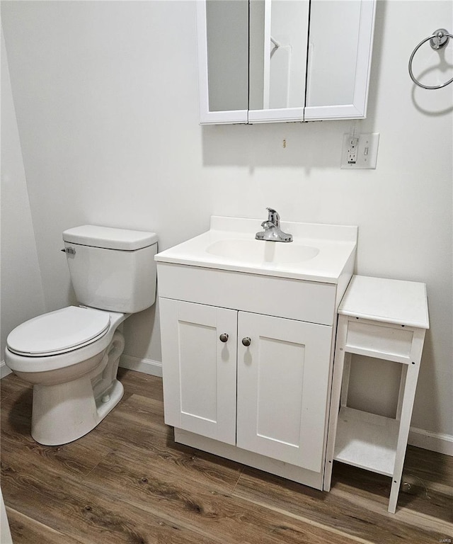 half bathroom with wood finished floors, baseboards, vanity, and toilet