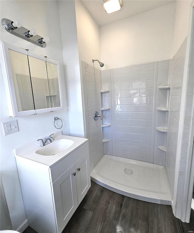 full bath with a tile shower, vanity, and wood finished floors