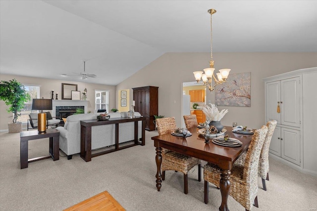 dining area with lofted ceiling, a premium fireplace, ceiling fan with notable chandelier, and light colored carpet