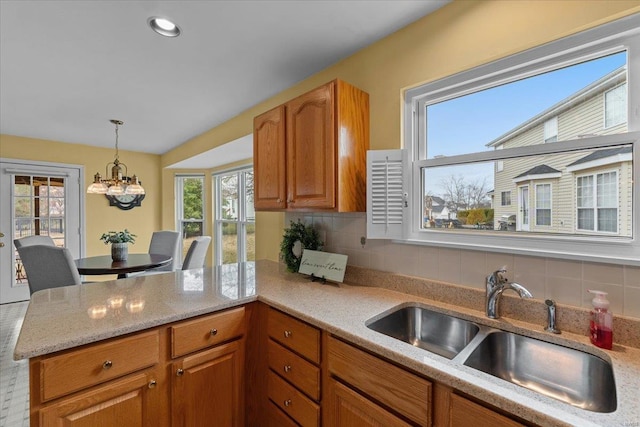 kitchen with decorative light fixtures, brown cabinets, decorative backsplash, a sink, and a peninsula