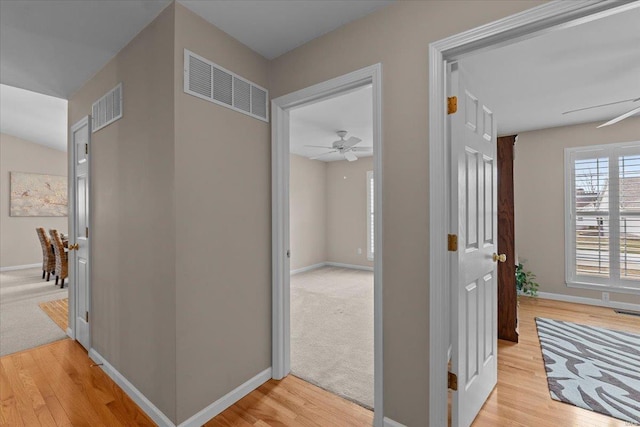 hall featuring baseboards, visible vents, and light wood-style floors