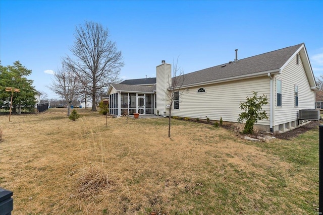 rear view of property featuring a sunroom, a lawn, a chimney, and central air condition unit