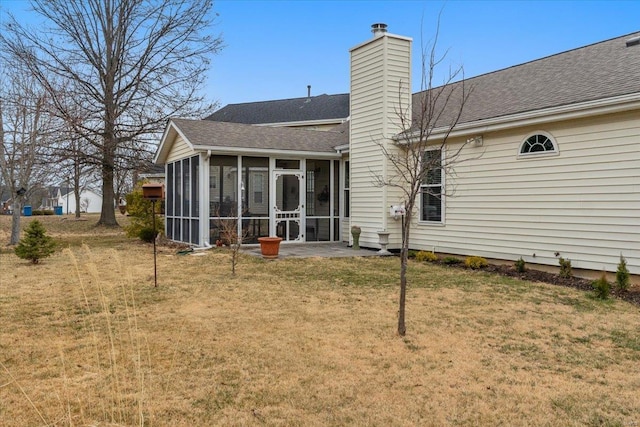 back of property featuring a sunroom, roof with shingles, a yard, and a chimney