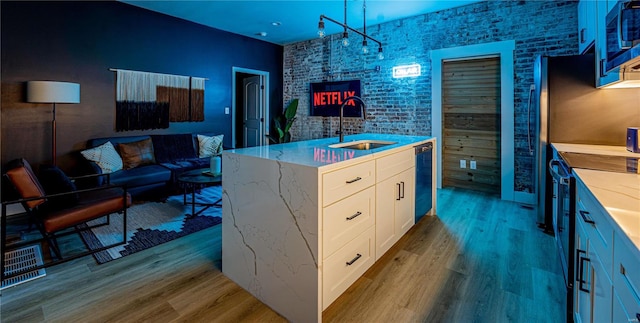 bar with light wood finished floors, dishwasher, built in microwave, pendant lighting, and a sink