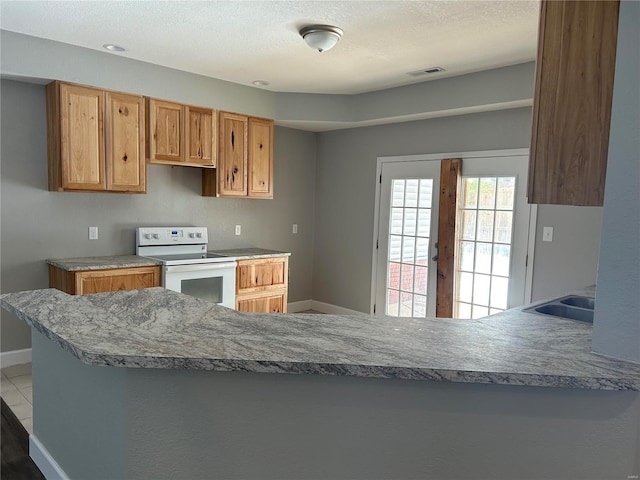 kitchen featuring baseboards, white electric range, visible vents, and a peninsula