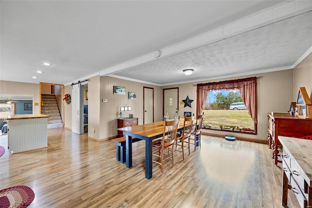 dining area featuring light wood-style floors, a barn door, stairs, and crown molding