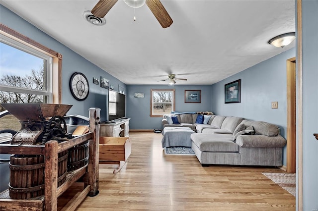 living area with visible vents, light wood-type flooring, a ceiling fan, and baseboards