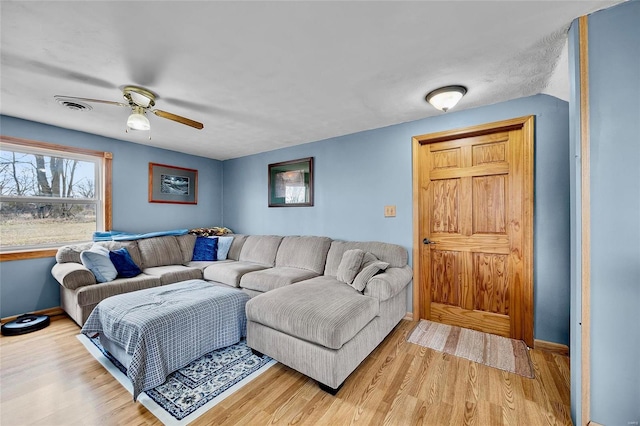 living area with light wood-style flooring, visible vents, ceiling fan, and baseboards