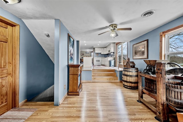 living area featuring light wood finished floors, visible vents, baseboards, ceiling fan, and stairway