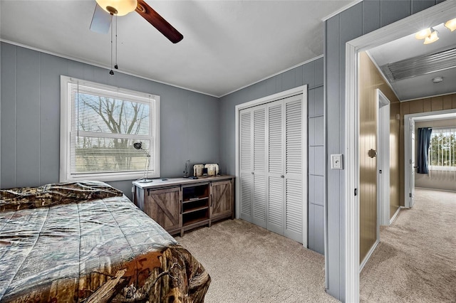 bedroom with light carpet, ceiling fan, a closet, and wooden walls