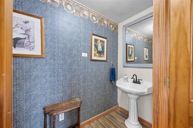 bathroom with a sink, wallpapered walls, baseboards, and wood finished floors