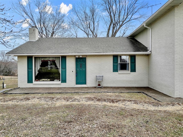 property entrance featuring roof with shingles, a chimney, and brick siding