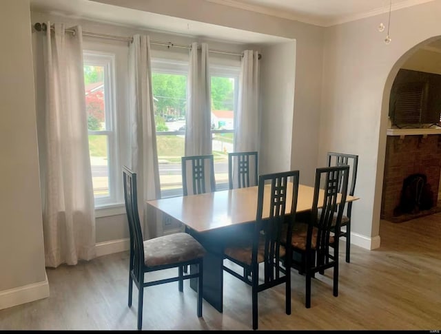 dining area with arched walkways, light wood-style flooring, a fireplace, baseboards, and crown molding