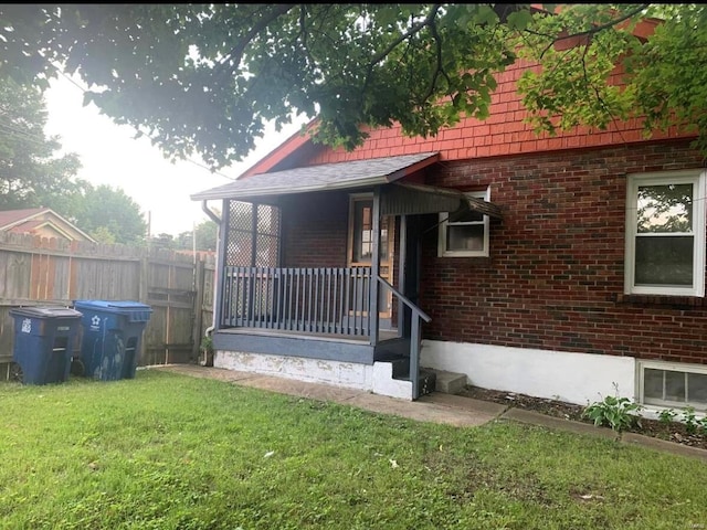 view of front facade featuring a porch, a front yard, brick siding, and fence