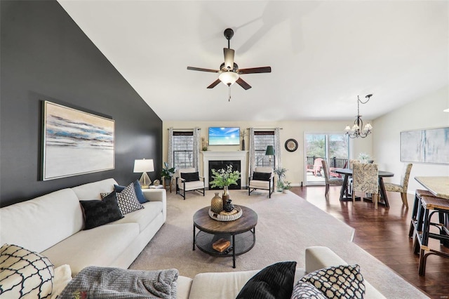 living area featuring a fireplace, vaulted ceiling, wood finished floors, baseboards, and ceiling fan with notable chandelier