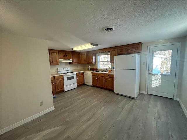 kitchen featuring white appliances, brown cabinetry, light wood-style floors, light countertops, and under cabinet range hood