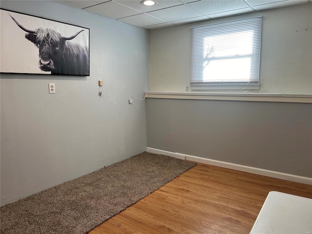 empty room featuring a drop ceiling, wood finished floors, and baseboards