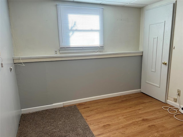 unfurnished room with light wood finished floors, a drop ceiling, and baseboards