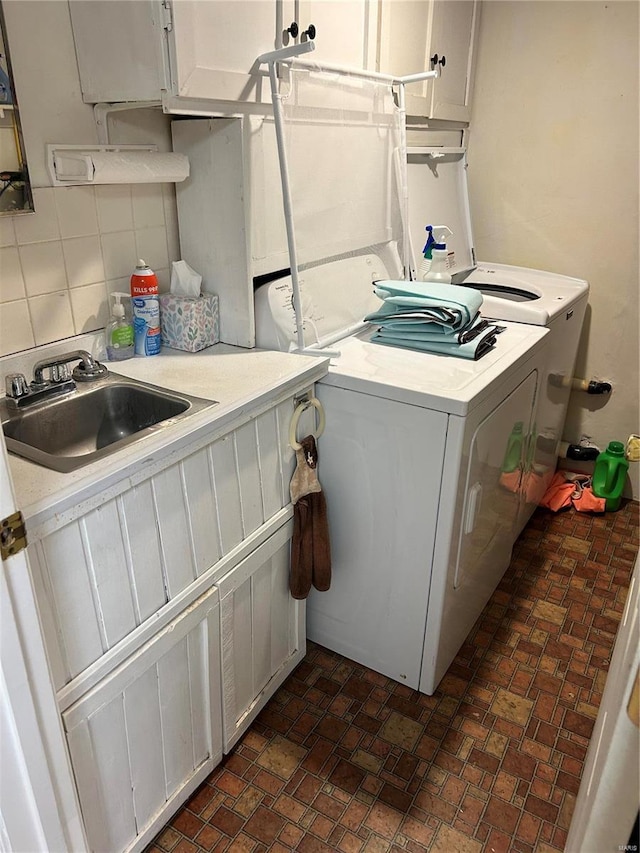 laundry room with brick floor, cabinet space, a sink, and washer and clothes dryer