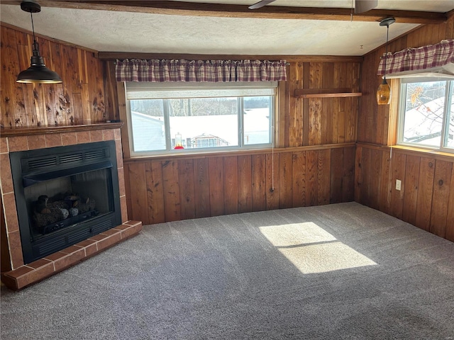 unfurnished living room featuring plenty of natural light, carpet, wood walls, and a textured ceiling