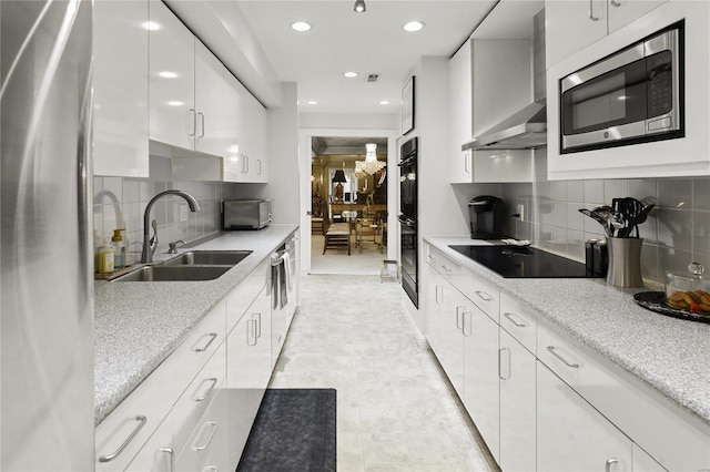 kitchen featuring recessed lighting, white cabinets, a sink, black appliances, and wall chimney exhaust hood