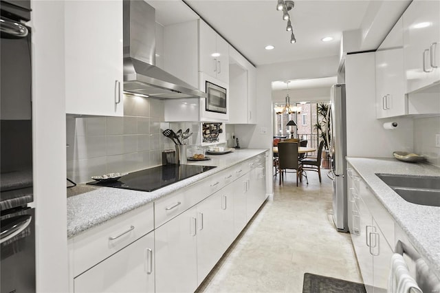 kitchen with appliances with stainless steel finishes, white cabinets, wall chimney range hood, and light stone countertops