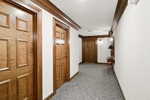 hallway with dark carpet, visible vents, crown molding, and baseboards