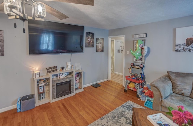 living area featuring a textured ceiling, a fireplace, baseboards, and wood finished floors