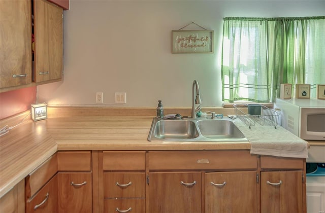 kitchen featuring brown cabinetry, light countertops, a sink, and white microwave