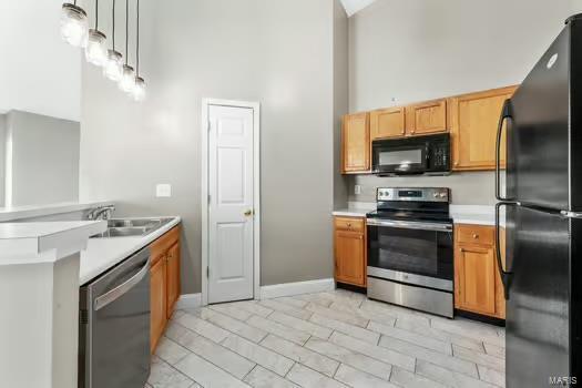 kitchen with a towering ceiling, baseboards, light countertops, black appliances, and pendant lighting