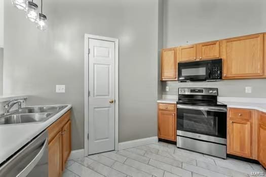 kitchen featuring a sink, baseboards, light countertops, appliances with stainless steel finishes, and pendant lighting