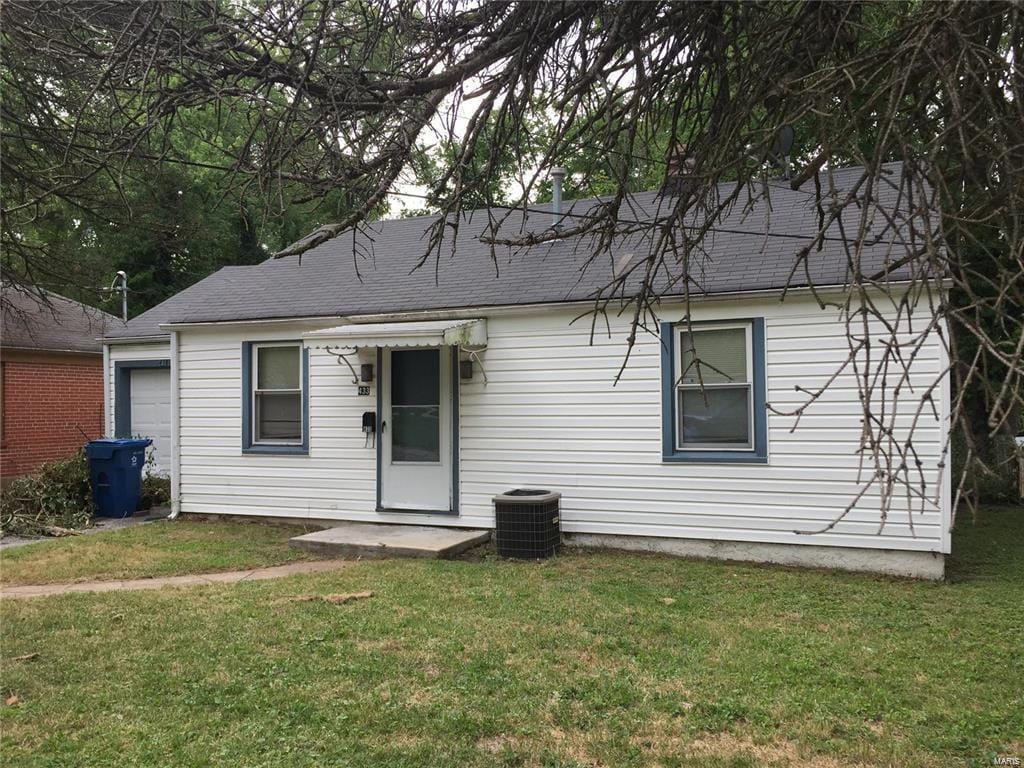 rear view of property with a shingled roof, cooling unit, and a yard