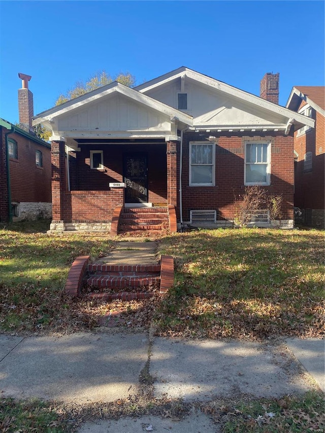 bungalow with board and batten siding, a front yard, brick siding, and a chimney