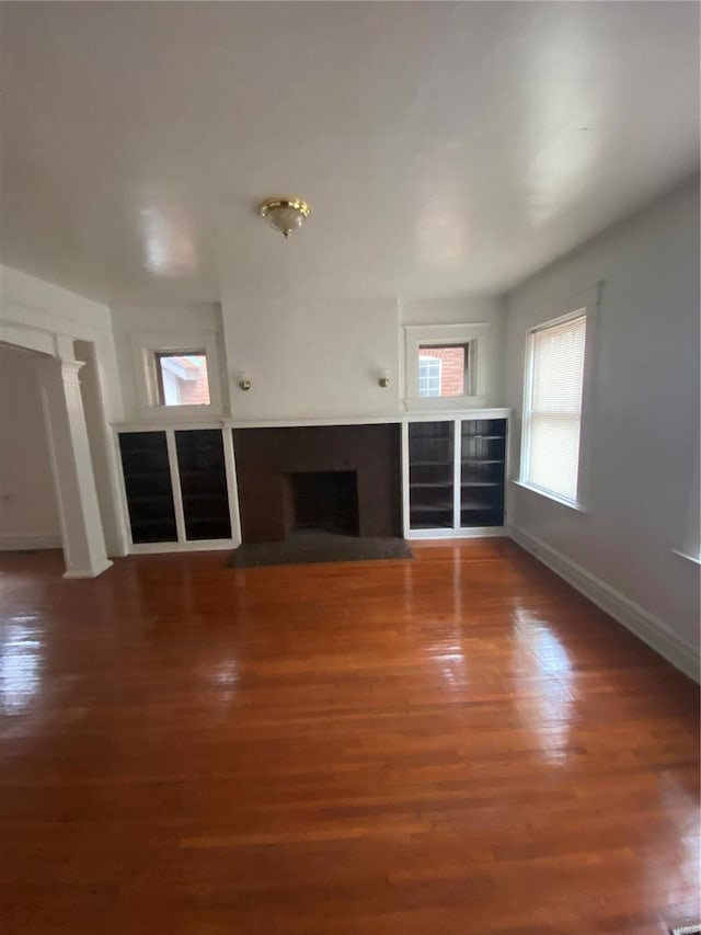 unfurnished living room featuring ornate columns, a fireplace with raised hearth, baseboards, and wood finished floors