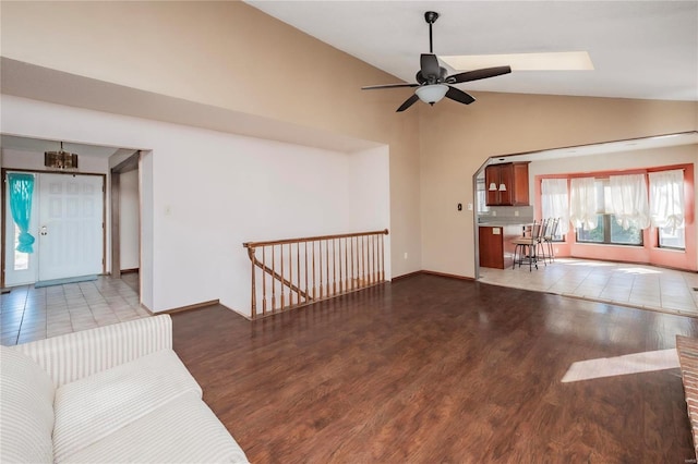 unfurnished living room featuring a ceiling fan, high vaulted ceiling, baseboards, and wood finished floors